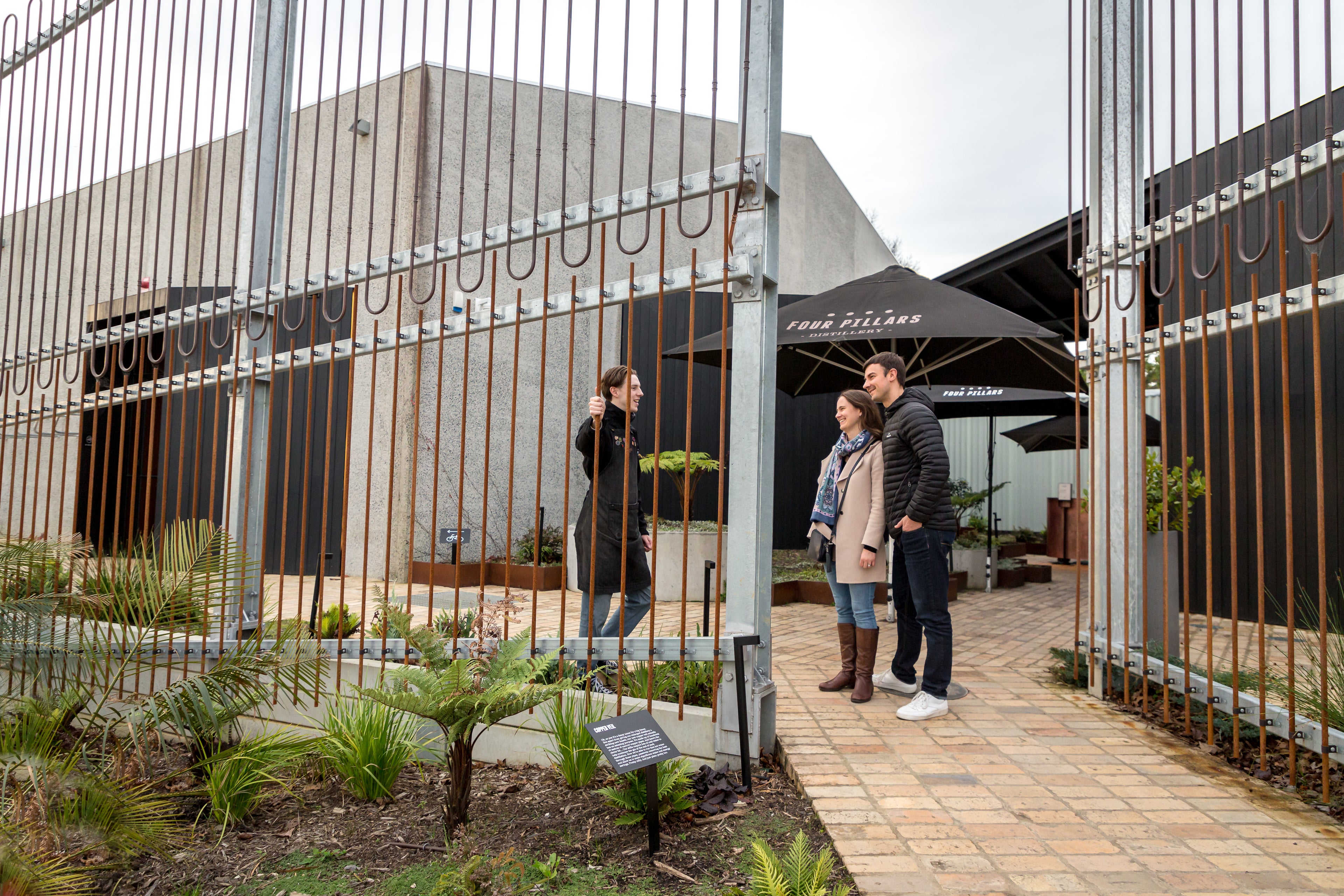 A couple visiting the Four Pillars Distillery is being shown the copper fence outside the building by a Four Pillars staff member.