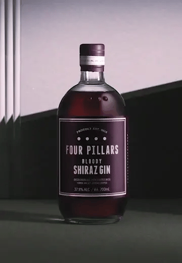 Red gin pouring over a bottle of a Four Pillars Gin Bloody Shiraz Gin
